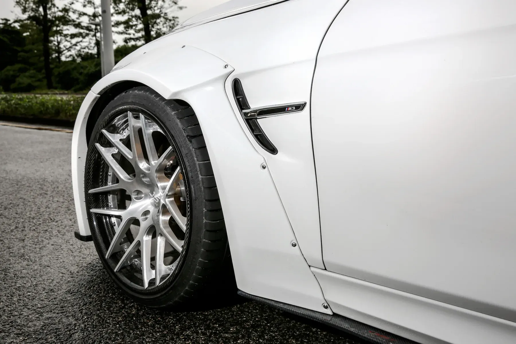 Close-up of a white BMW 3 Series front arch, riveted arch extension with the tire shoulder and tread inside the lip
