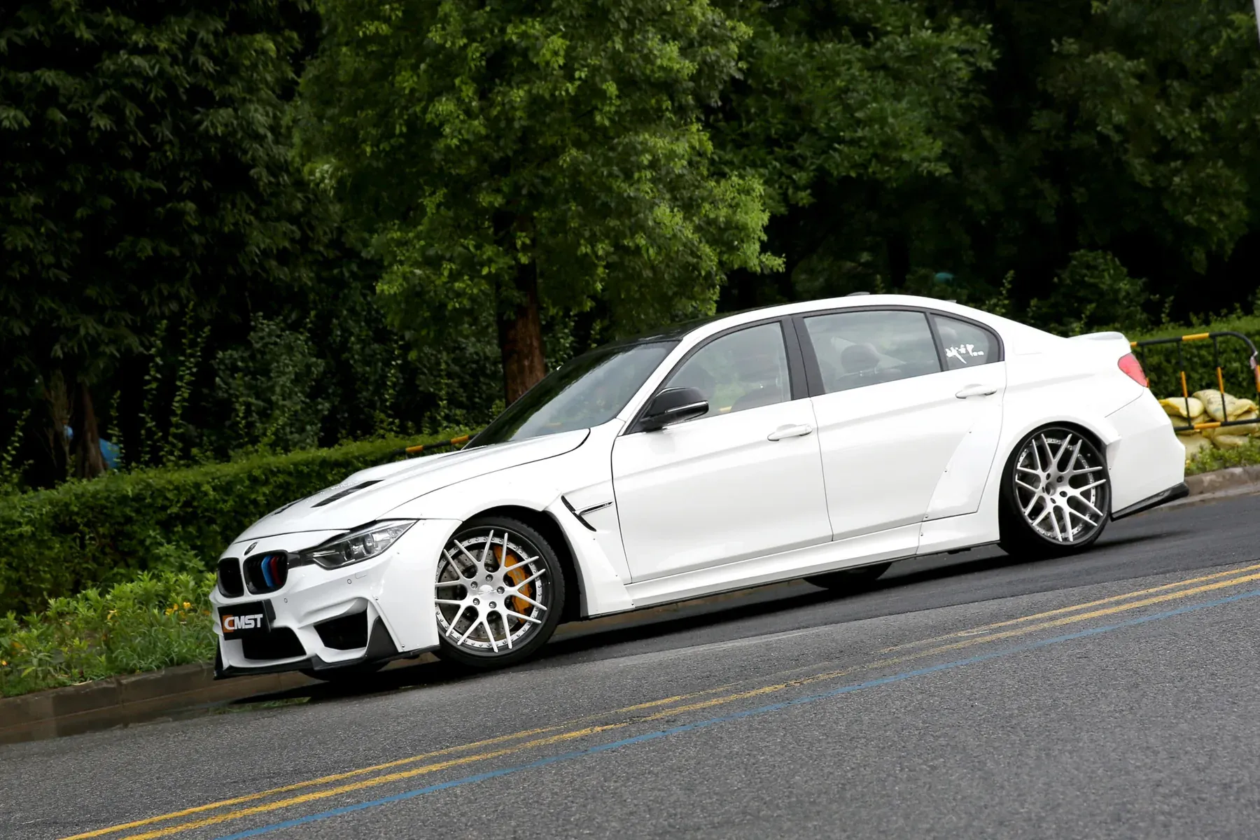 White BMW 3 Series with widened arches, side skirts and a deeper front bumper, parked on a road