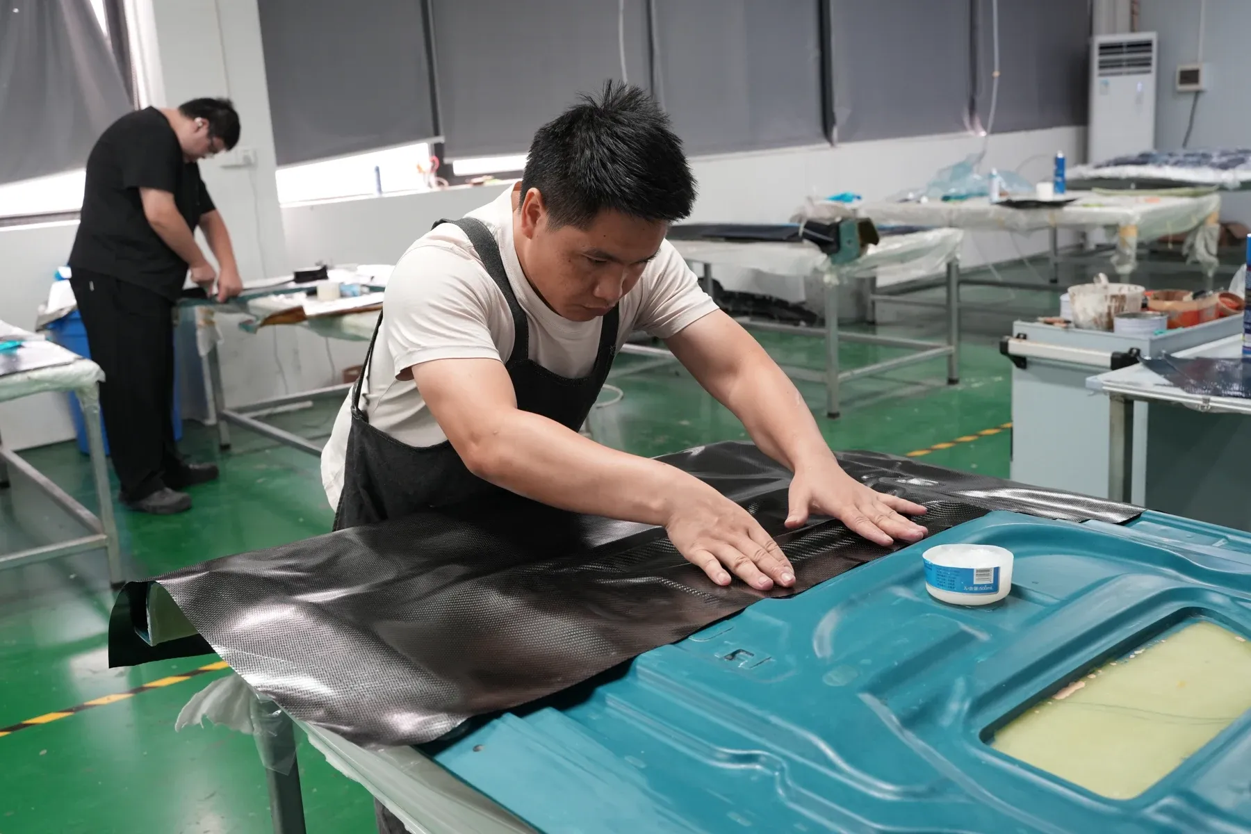 Technician laying carbon cloth over a hood mold before the part is vacuum bagged and cured