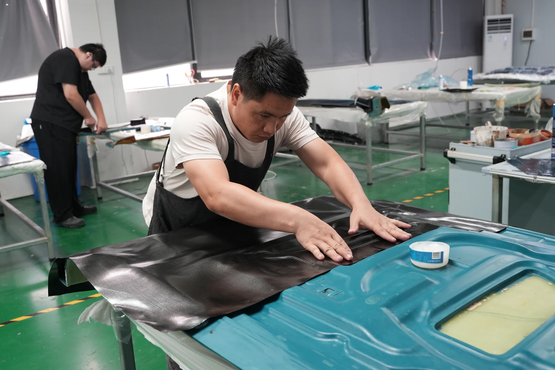 Workshop technician laying carbon fiber sheet into a mold with vacuum bagging film over it