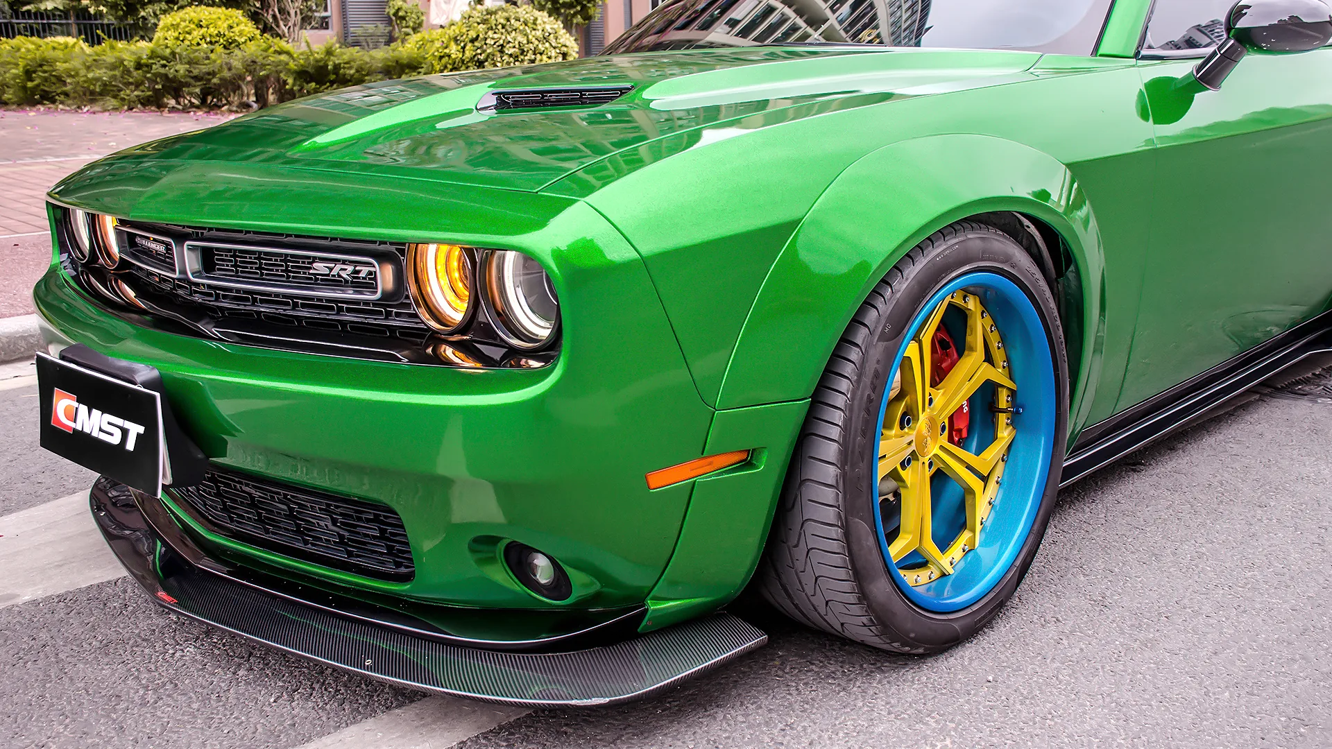 Green Dodge Challenger front corner in close-up, with a carbon fiber front lip under the bumper, a black side skirt along the sill and a wide wheel and tire package