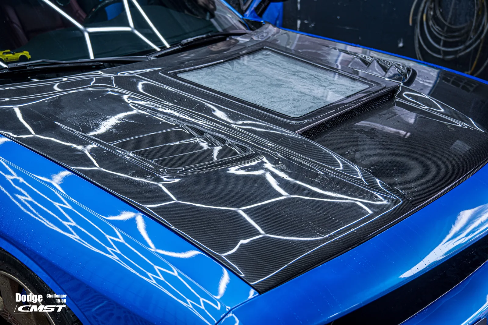Blue Dodge Challenger with a carbon fiber hood fitted with a clear centre window, photographed from the front left at close range