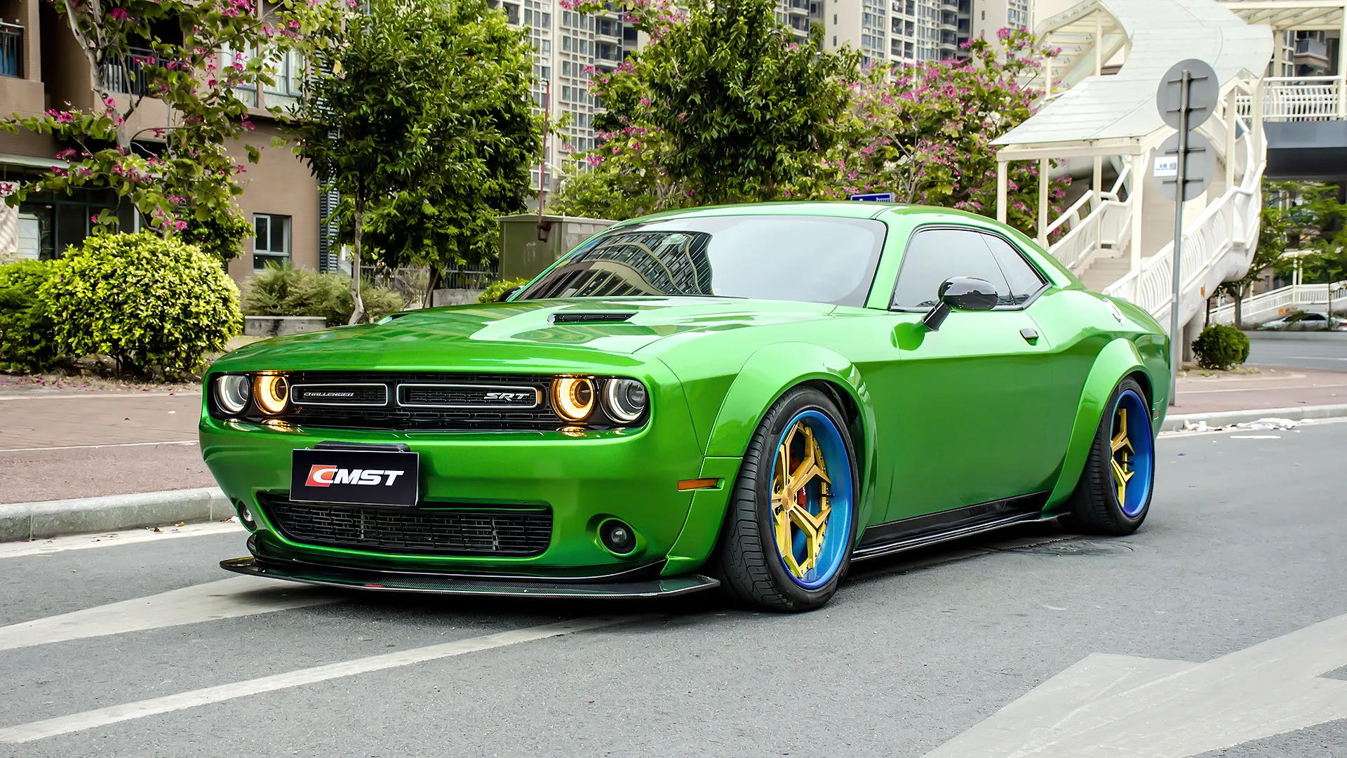 Green Dodge Challenger with a carbon front lip and black side skirts, parked on a city street