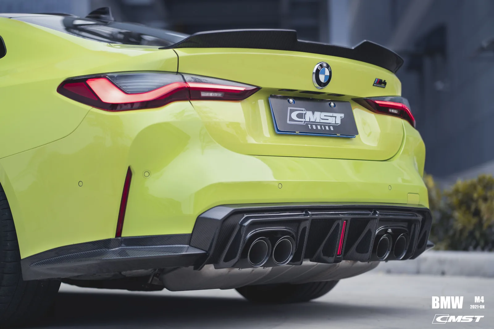 Rear three-quarter view of a yellow BMW M4 G82 showing the carbon rear diffuser, quad exhausts and trunk spoiler