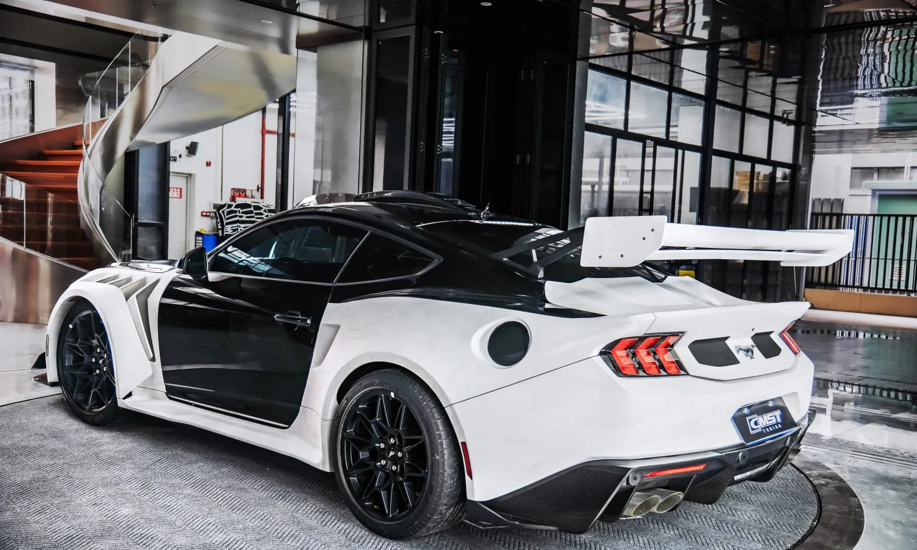 A white sports car with wide rear arches and a wide rear wing, photographed indoors