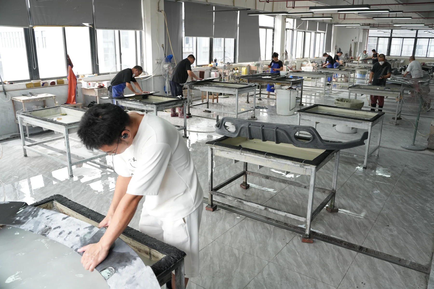 Workers wet-sanding carbon fiber panels at benches on the finishing floor