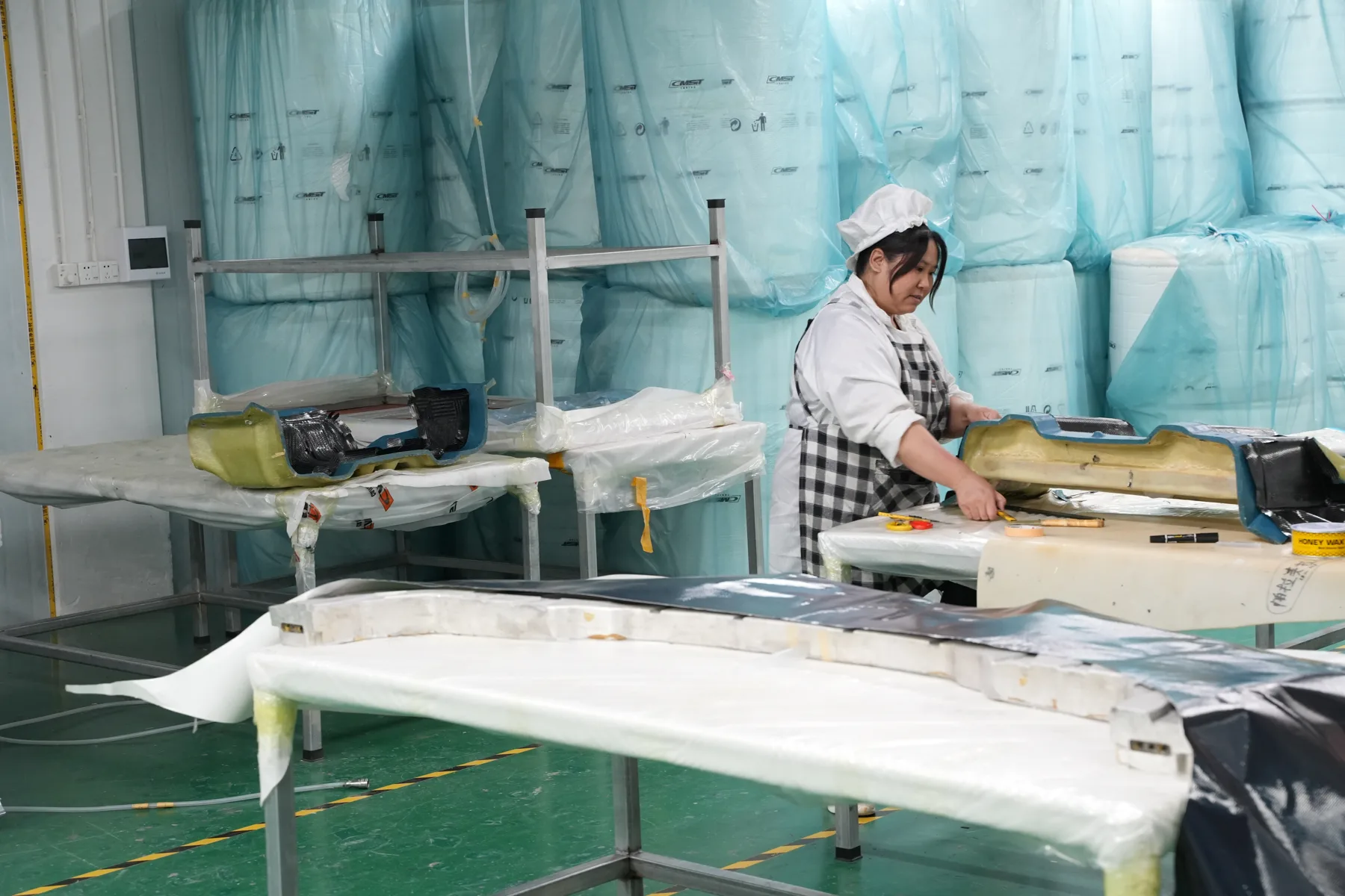 Carbon parts sealed in vacuum bag film on racks behind a technician at a lay-up bench